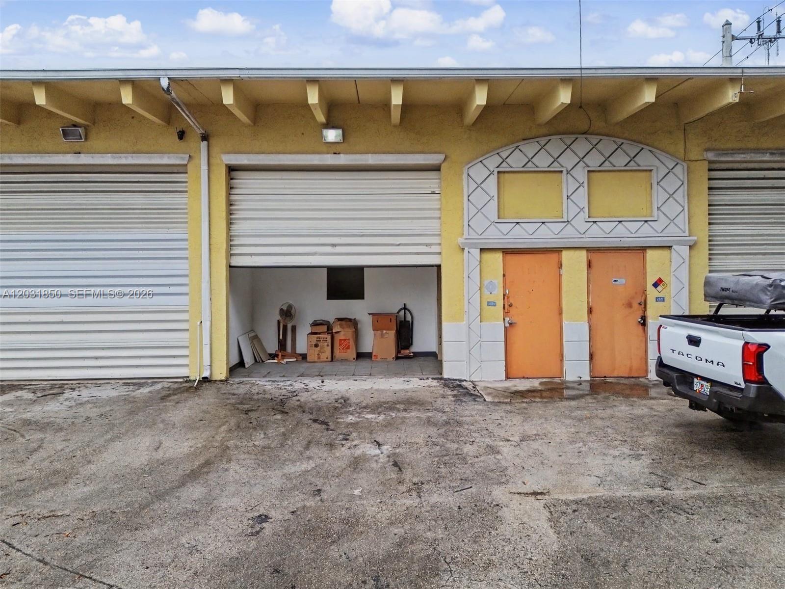 A commercial building exterior features a roll-up bay door, two orange doors, and a truck — 2225 SW 57th Ave # 2, West Park FL 33023, WEST PARK, FL
