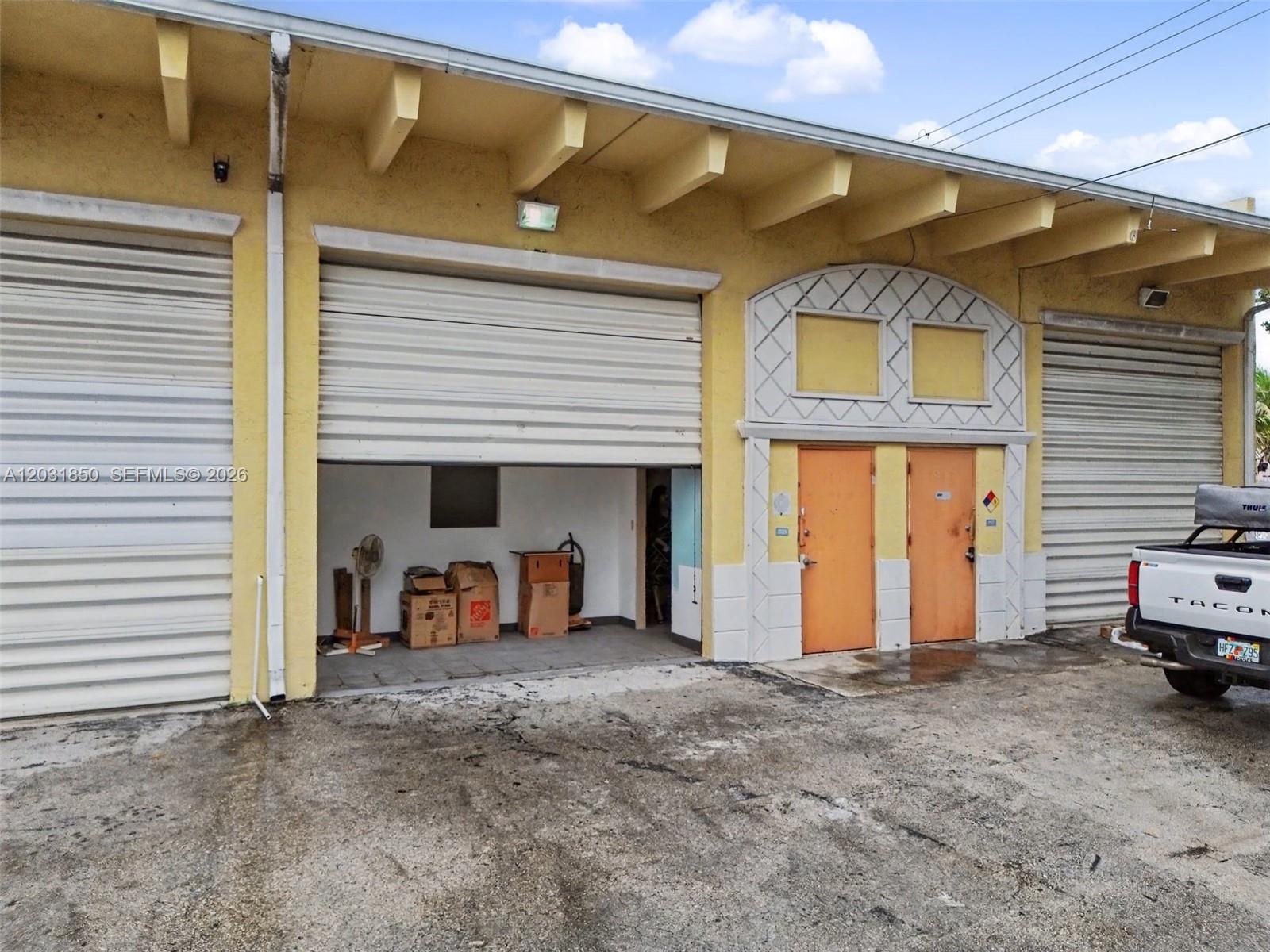 An exterior view of a commercial building with roll-up doors, two orange doors, and boxes — 2225 SW 57th Ave # 2, West Park FL 33023, WEST PARK, FL