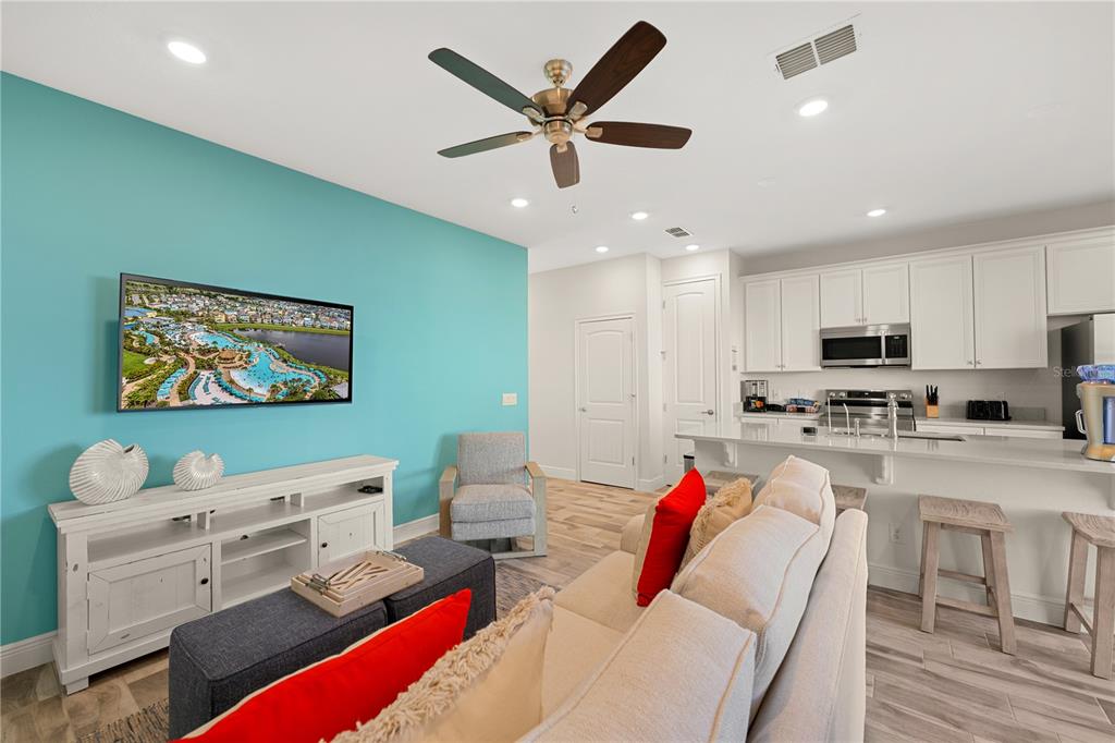 A living room with a teal accent wall, white media console, and an open kitchen — 8205 SURF STREET, KISSIMMEE, FL