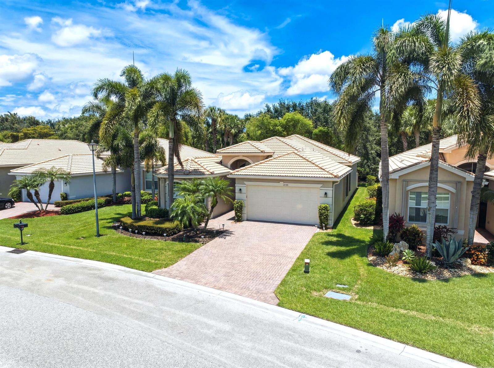 An aerial view of a suburban house with a tiled roof, brick driveway, and palm trees — 10588 Stone Garden Drive, Boynton Beach FL 33473, BOYNTON BEACH, FL