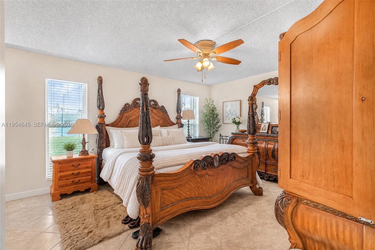 A bedroom features a large wooden four-poster bed, tiled floors, and a ceiling fan — 1521 NW 18th AVE # 101, Delray Beach FL 33445, DELRAY BEACH, FL