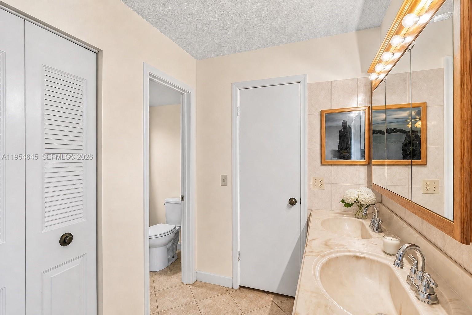 A bathroom features a double vanity with beige countertops, tile walls, and a separate toilet area — 1521 NW 18th AVE # 101, Delray Beach FL 33445, DELRAY BEACH, FL