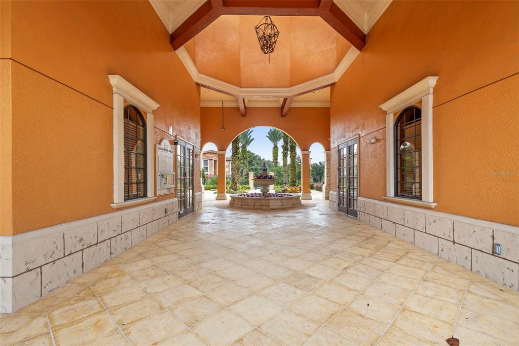 An outdoor covered walkway features a central fountain, stone tile flooring, and orange stucco walls — 6135 METROWEST BOULEVARD UNIT 105, ORLANDO, FL