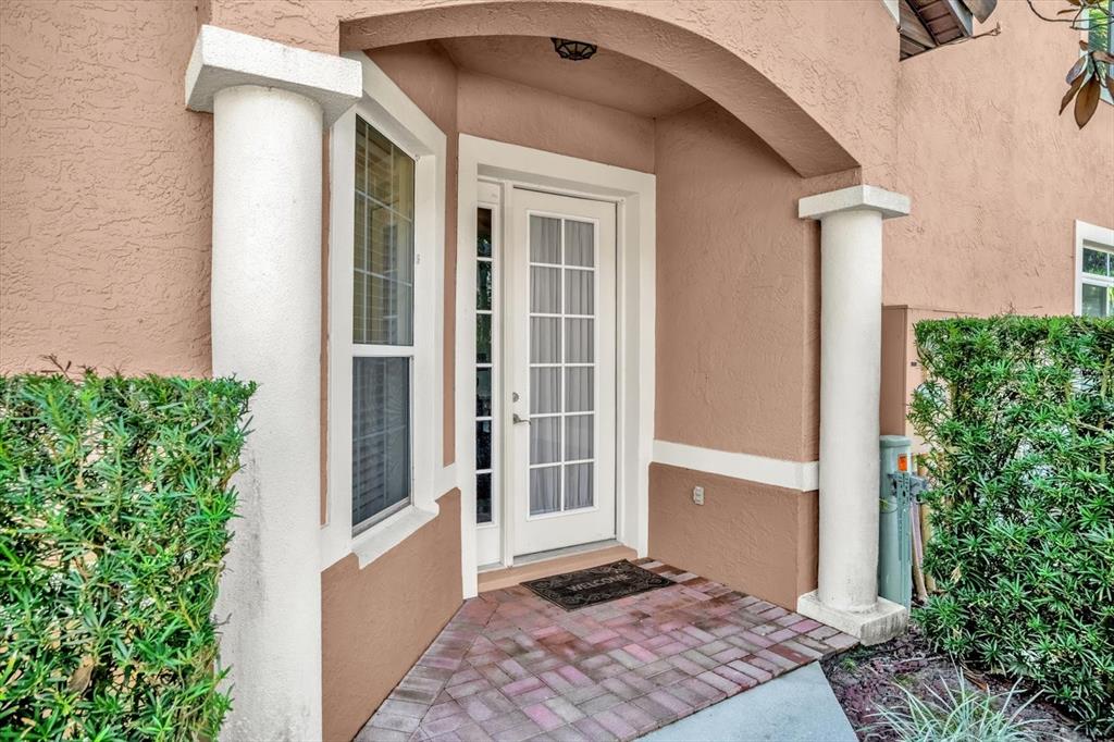 A tan stucco home entrance features a white front door, columns, and brick pavers — 202 CAMINO REAL BOULEVARD UNIT 202, HOWEY IN THE HILLS, FL