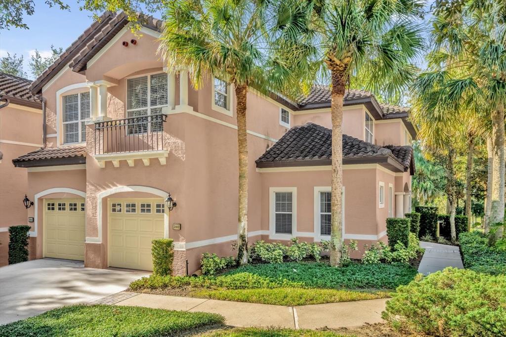 A two-story stucco house with a two-car garage, a balcony, and palm trees in front — 202 CAMINO REAL BOULEVARD UNIT 202, HOWEY IN THE HILLS, FL
