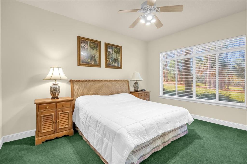 A bedroom with green carpet, a wicker headboard, white bedding, and a ceiling fan — 202 CAMINO REAL BOULEVARD UNIT 202, HOWEY IN THE HILLS, FL