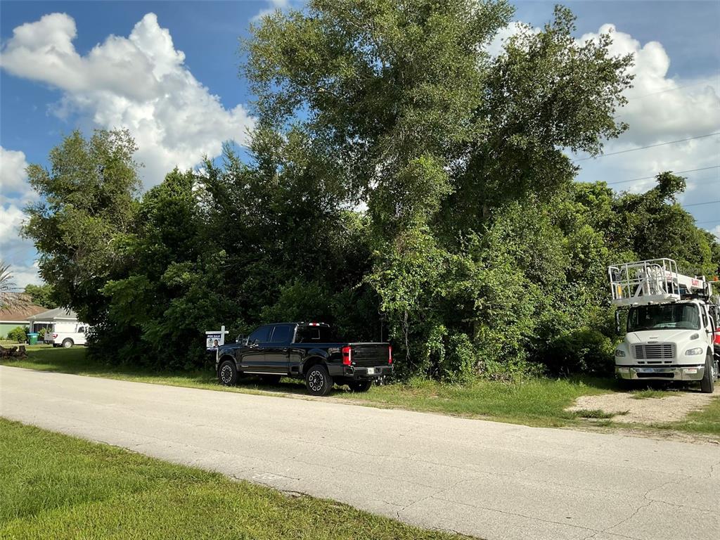 A black pickup truck and a bucket truck are parked in front of a wooded lot — 883 TRUMBULL STREET, DELTONA, FL
