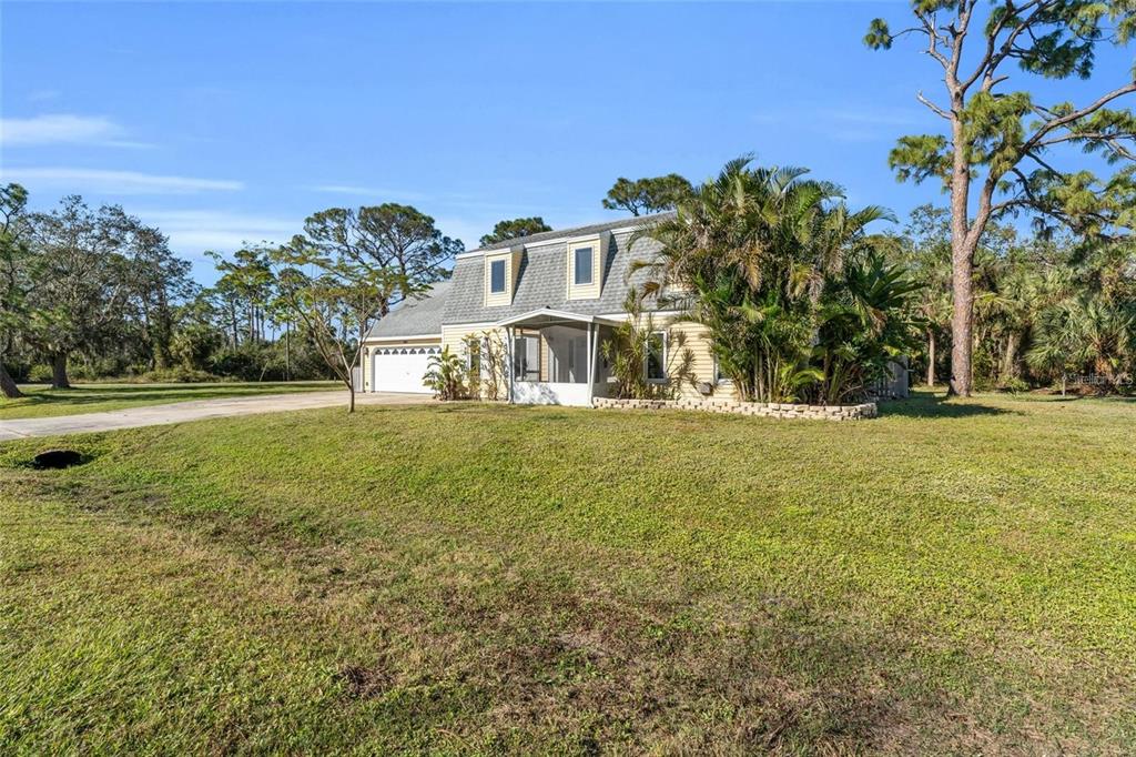 A two-story house with a gambrel roof and a screened porch sits on a grassy lot — 17402 BILLIAR AVENUE, PORT CHARLOTTE, FL