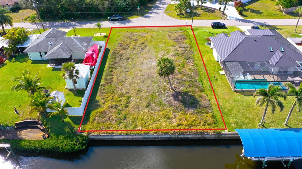 An aerial view shows a vacant, rectangular waterfront lot outlined in red between two houses — 3454 YUKON DRIVE, PORT CHARLOTTE, FL