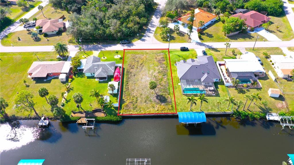 An aerial view shows a vacant waterfront lot outlined in red between two residential houses — 3454 YUKON DRIVE, PORT CHARLOTTE, FL