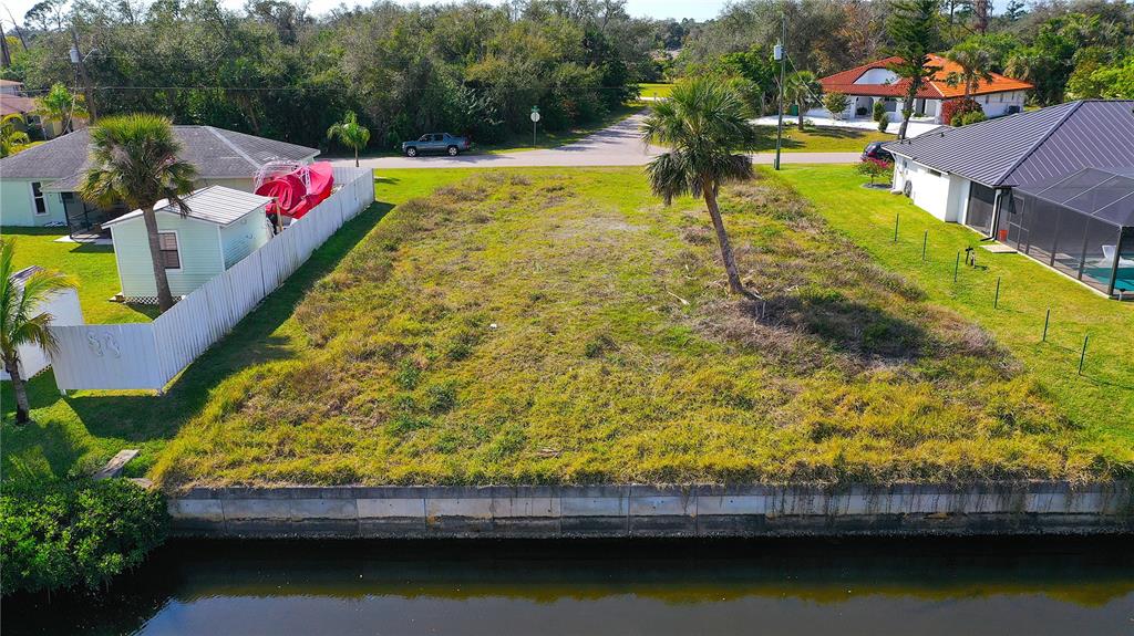 An aerial view shows a vacant, grassy waterfront lot situated between two residential houses — 3454 YUKON DRIVE, PORT CHARLOTTE, FL