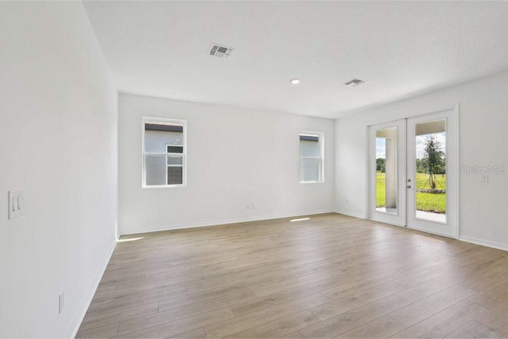 An empty room with white walls, light wood-look flooring, two windows, and glass patio doors — 30135 EMERALD FOREST DRIVE, MOUNT DORA, FL