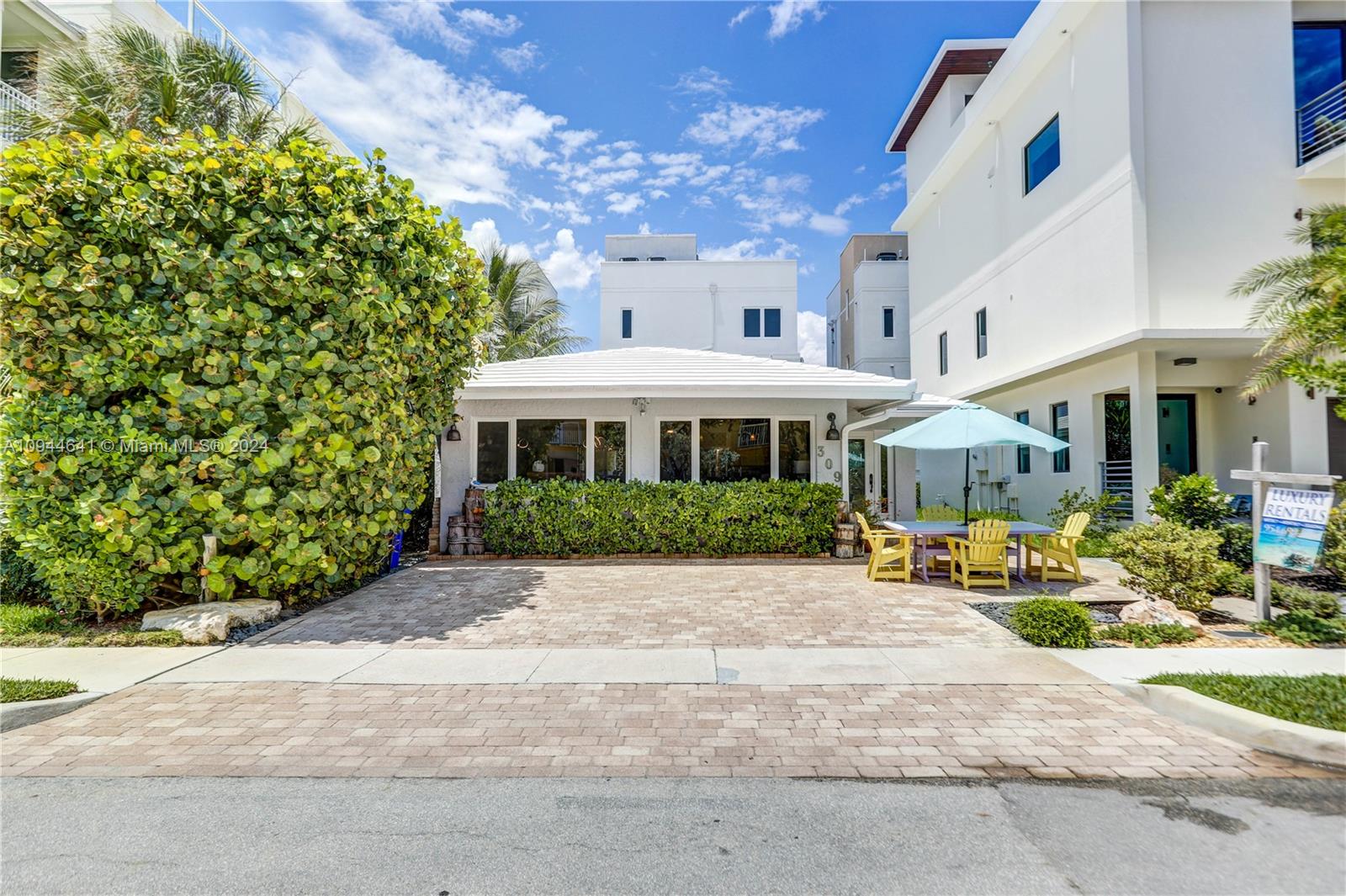 A paved driveway leads to a single-story house with a white roof and outdoor seating — 309 Oak St, Hollywood FL 33019, HOLLYWOOD, FL