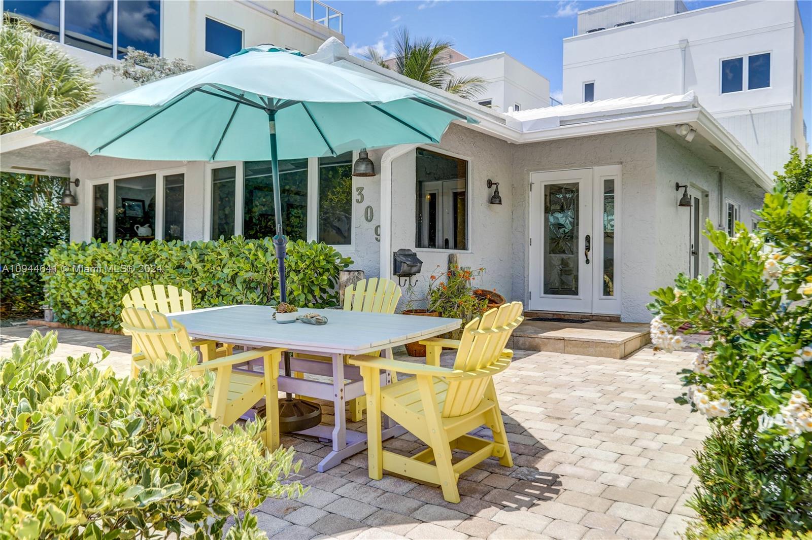 A patio with a dining set and umbrella sits in front of a white house — 309 Oak St, Hollywood FL 33019, HOLLYWOOD, FL