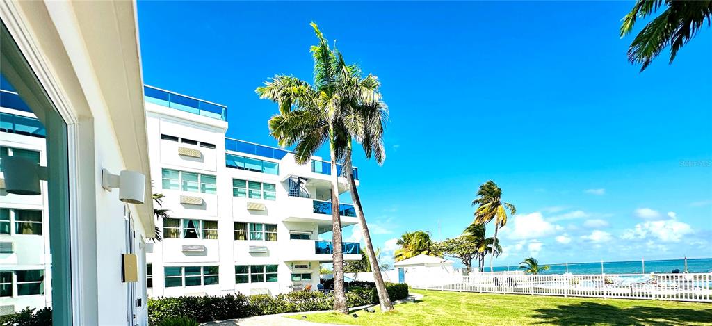 A white multi-story building stands beside a palm tree overlooking the ocean — COND COSTAMAR BEACH VILLAGE UNIT CO-203, LOIZA, PR