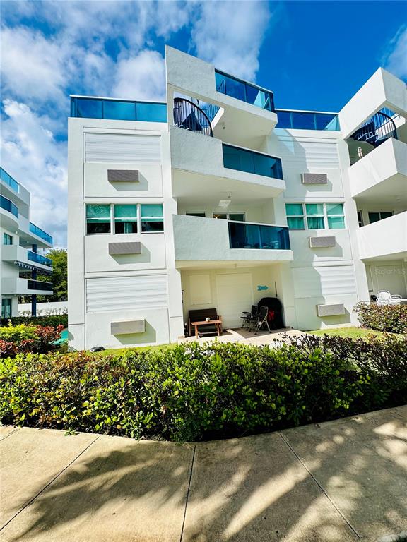 A multi-story white apartment building features balconies with glass railings and a ground-level patio area — COND COSTAMAR BEACH VILLAGE UNIT CO-203, LOIZA, PR