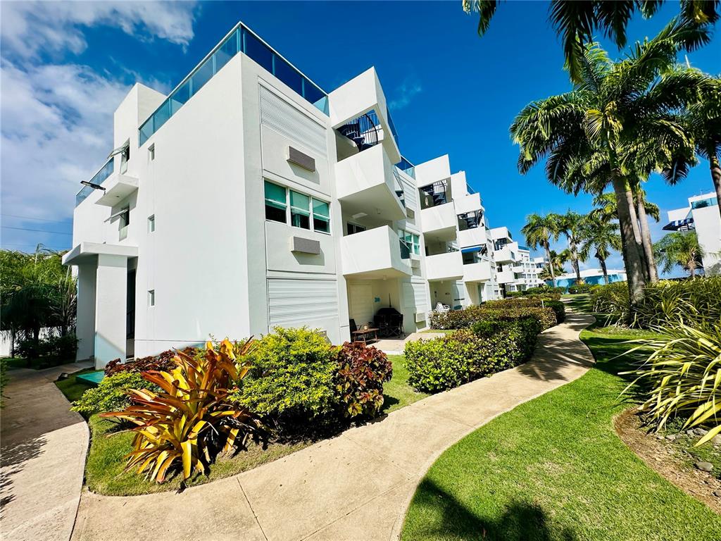 A multi-story white apartment building features balconies and a landscaped walkway under a blue sky — COND COSTAMAR BEACH VILLAGE UNIT CO-203, LOIZA, PR