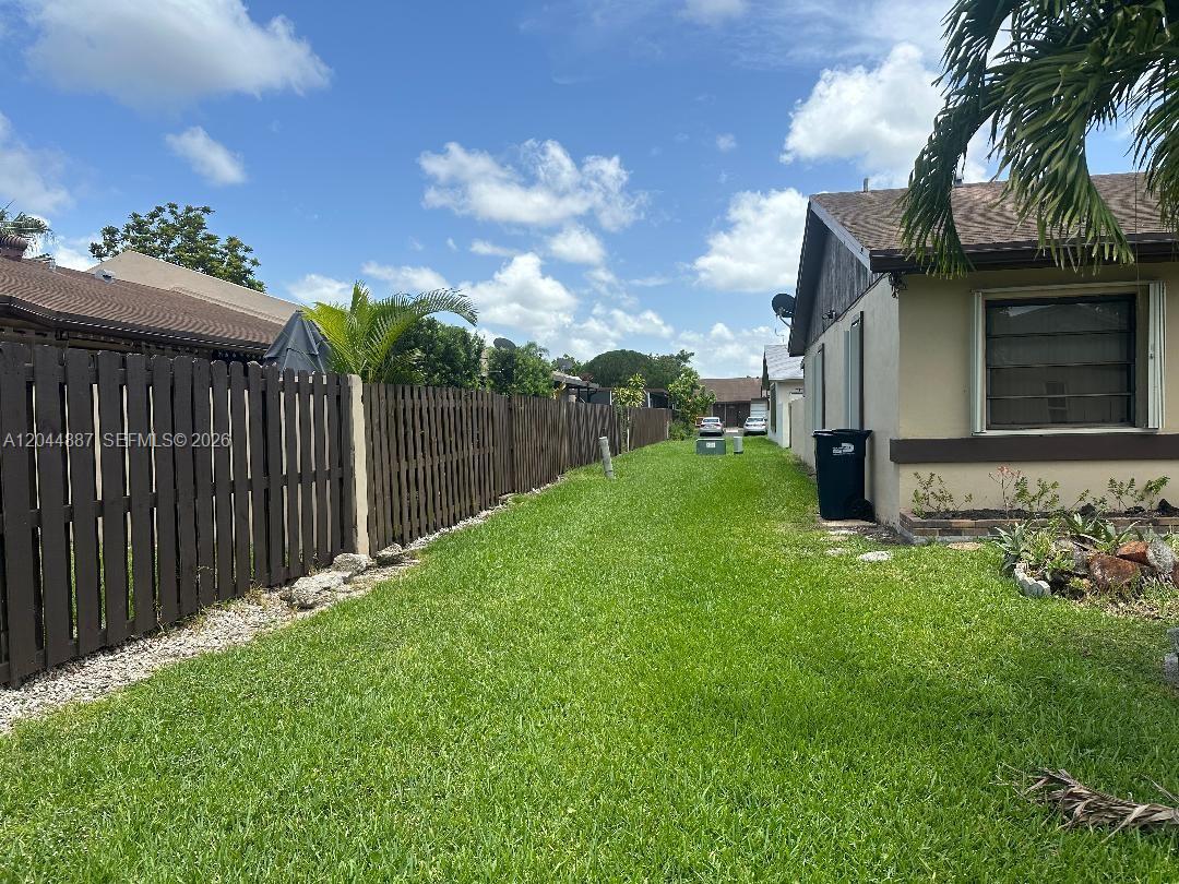 A side yard features a wooden fence, green grass, and the exterior of a house — MIAMI, FL