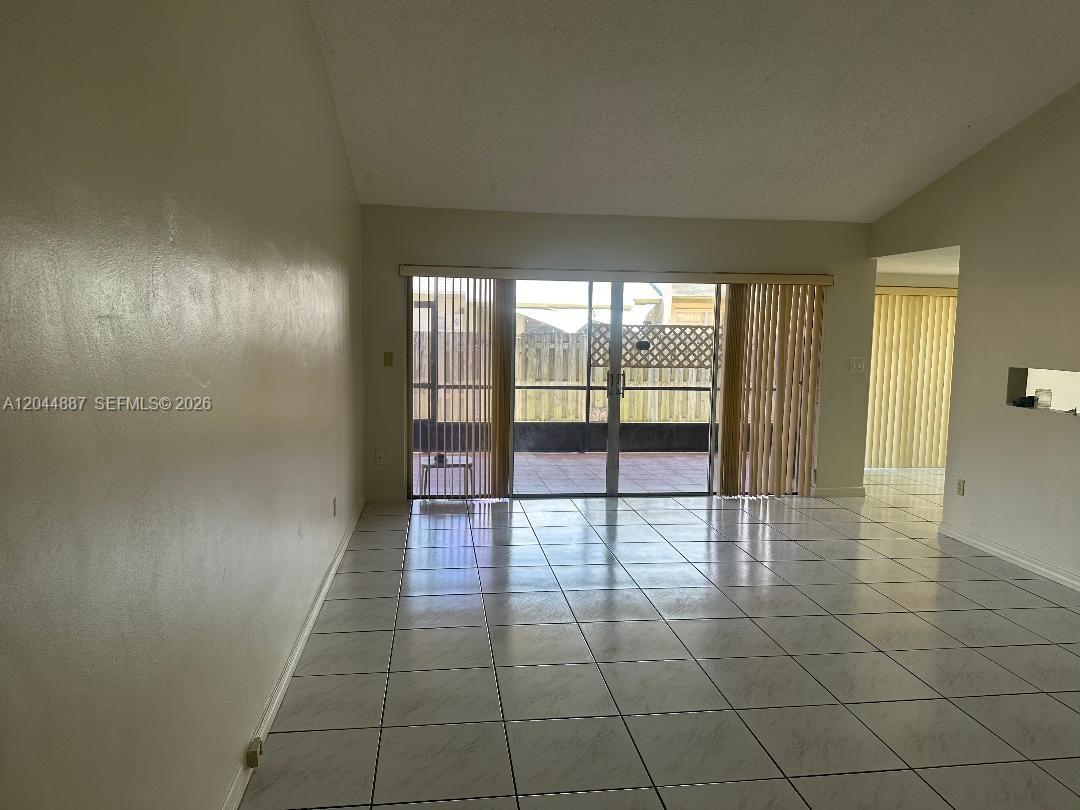 An empty room features white tiled floors, beige walls, and sliding glass doors to a patio — MIAMI, FL