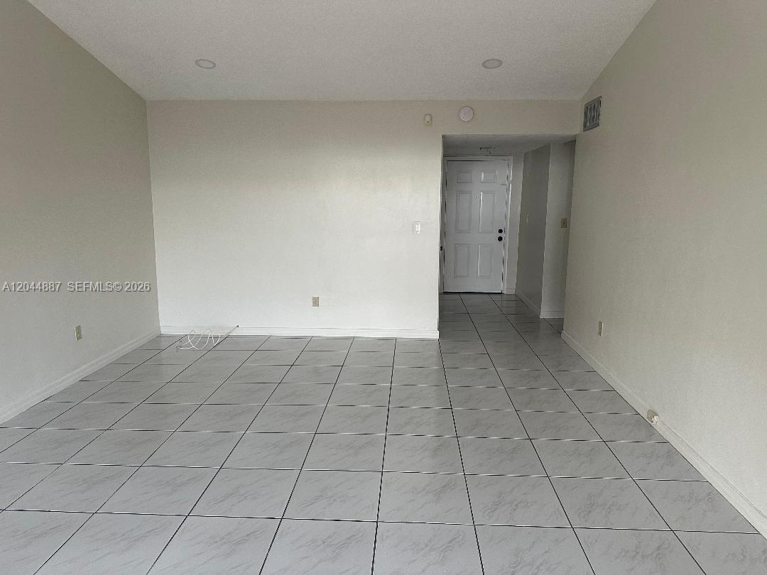 An empty room features light-colored tile flooring, plain walls, and a white entry door — MIAMI, FL