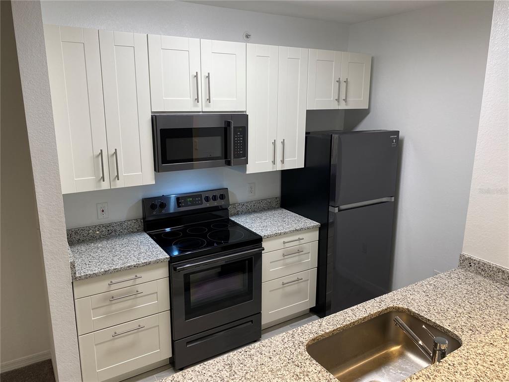 A kitchen features white shaker cabinets, granite countertops, and black appliances — 5455 VINELAND ROAD UNIT 3310, ORLANDO, FL