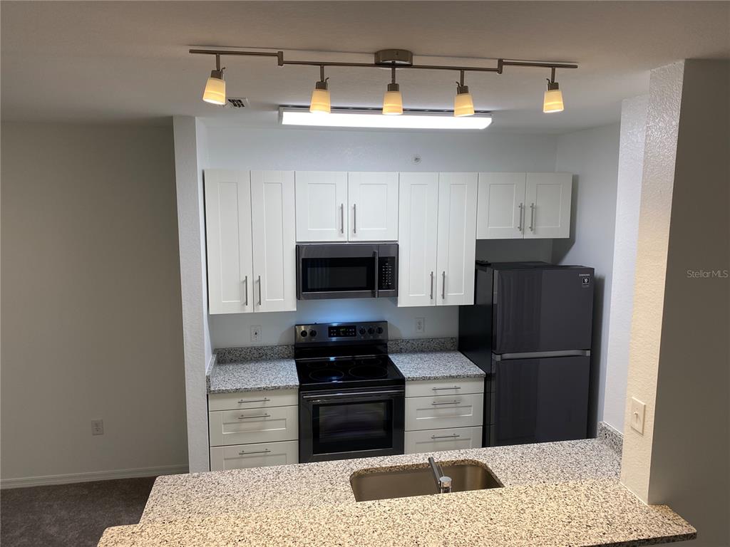 A kitchen features white cabinets, granite countertops, stainless steel appliances, and a track lighting fixture — 5455 VINELAND ROAD UNIT 3310, ORLANDO, FL