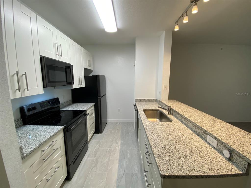 A kitchen features white cabinets, granite countertops, black appliances, and light-colored tile flooring — 5455 VINELAND ROAD UNIT 3310, ORLANDO, FL