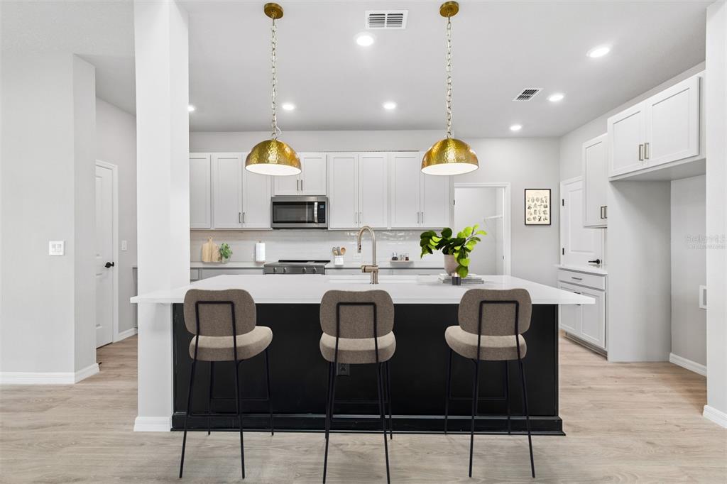 A modern kitchen features white cabinets, stainless steel appliances, a kitchen island, and light flooring — 15239 EASTLYN DRIVE, BRADENTON, FL