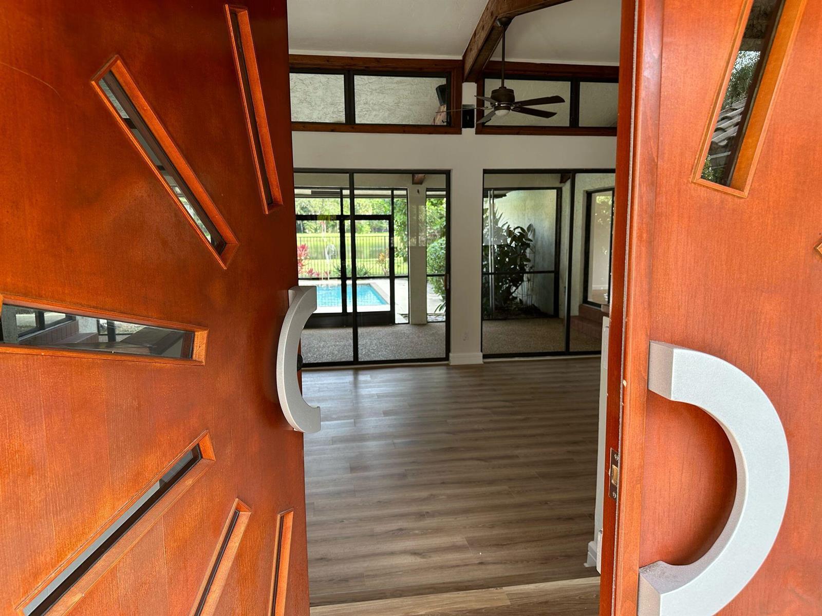 A view through open wooden doors into a room with wood flooring and pool access — 7243 Encina Lane, Boca Raton FL 33433, BOCA RATON, FL