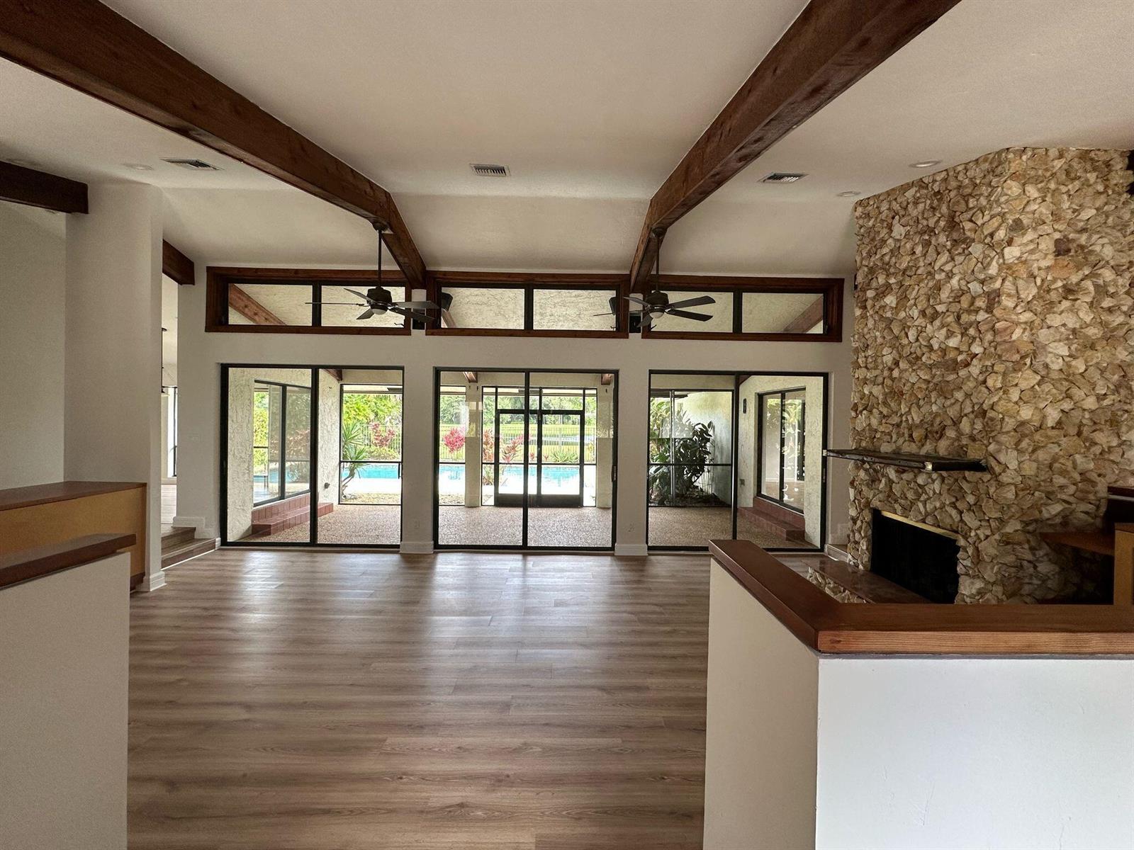 A living room features vaulted ceilings with exposed beams, a stone fireplace, and glass doors — 7243 Encina Lane, Boca Raton FL 33433, BOCA RATON, FL