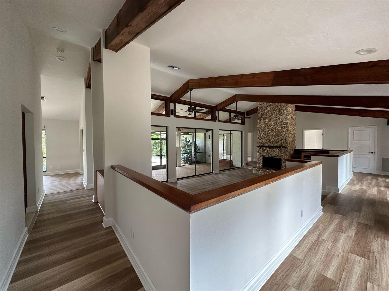 A living area with vaulted ceilings, exposed wood beams, stone fireplace, and wood-look flooring — 7243 Encina Lane, Boca Raton FL 33433, BOCA RATON, FL
