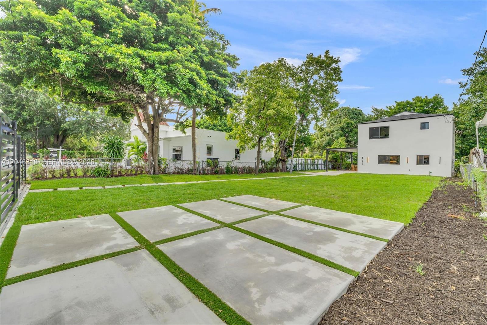 A backyard features a concrete paver patio, a grassy lawn, and two white buildings — 411 NW 59th St, Miami FL 33127, MIAMI, FL
