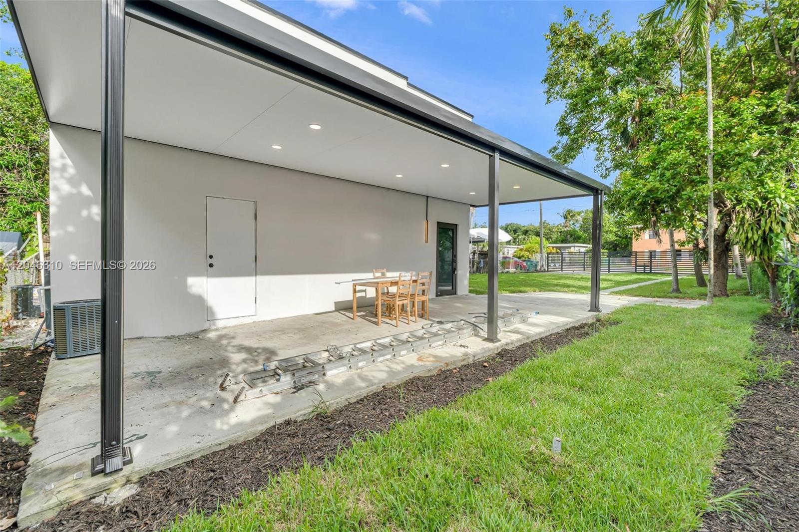 A covered concrete patio features a dining set, recessed lighting, and a metal ladder — 411 NW 59th St, Miami FL 33127, MIAMI, FL
