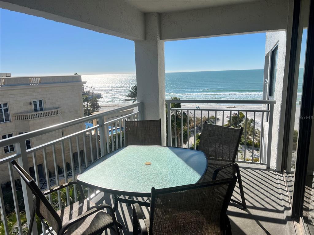 A balcony with a glass-topped table and chairs overlooks the ocean and a beach — 1001 POINT OF ROCKS ROAD UNIT 609, SARASOTA, FL
