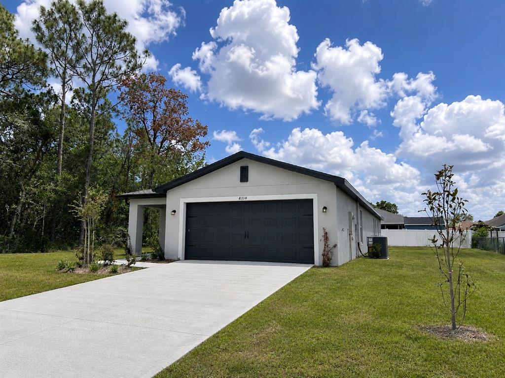 A single-story house with a gray exterior, dark garage door, and concrete driveway under a sky — 8338 CORAL STREET, SPRING HILL, FL