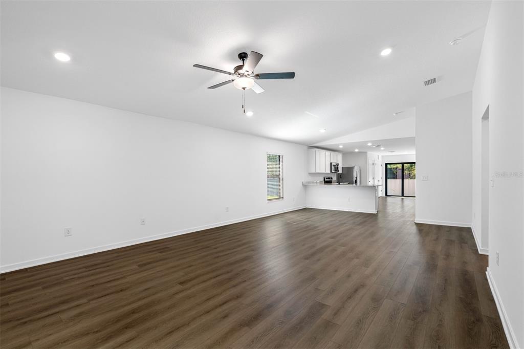 A spacious living room with dark wood-look flooring, a ceiling fan, and an open kitchen — 8338 CORAL STREET, SPRING HILL, FL