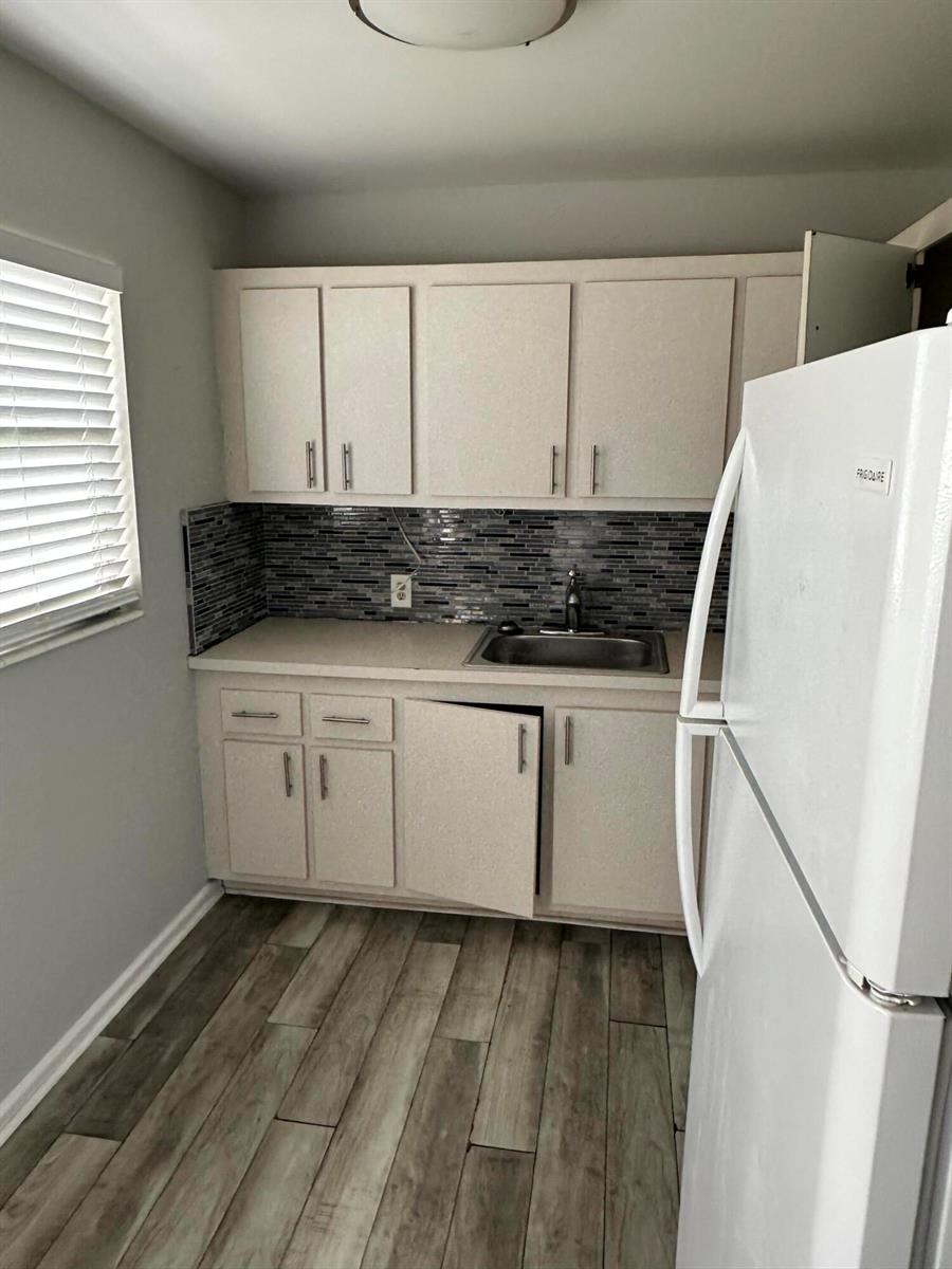 A small kitchen features white cabinets, a stainless steel sink, and a gray tiled backsplash — 599 Fanshaw O, Boca Raton FL 33434, BOCA RATON, FL