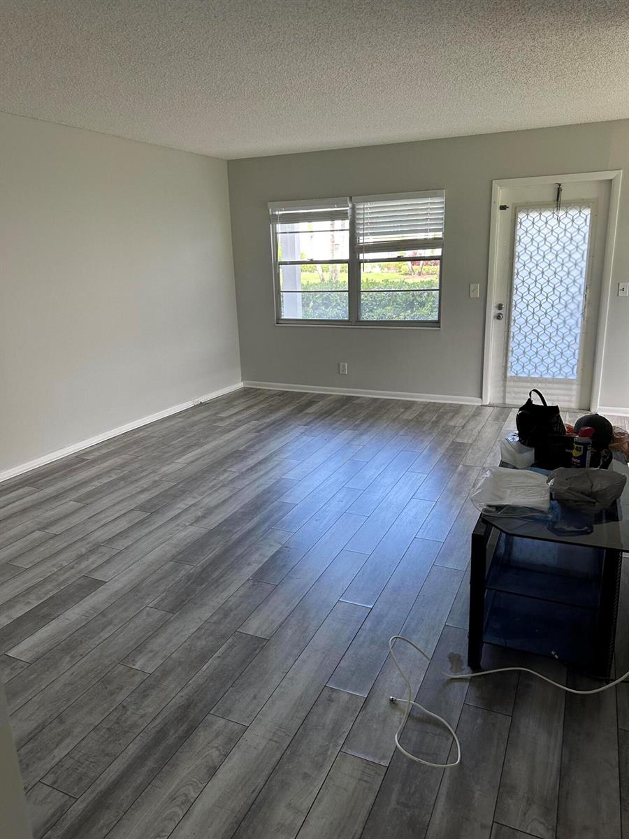 An empty living room features gray wood-look flooring, light gray walls, and a glass-paned door — 599 Fanshaw O, Boca Raton FL 33434, BOCA RATON, FL