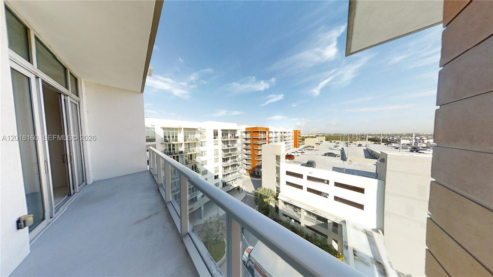 A balcony with a glass railing overlooks a parking garage and adjacent apartment buildings — 7825 NW 107th Ave # 821, Doral FL 33178, DORAL, FL