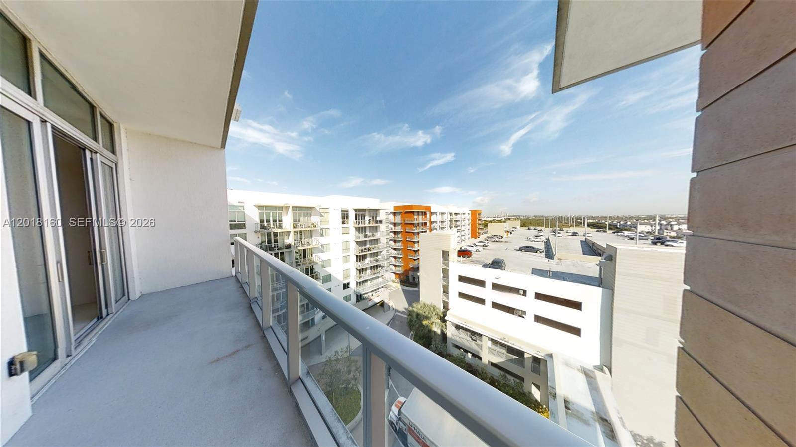 A balcony overlooks a parking garage and adjacent apartment buildings under a clear blue sky — 7825 NW 107th Ave # 821, Doral FL 33178, DORAL, FL