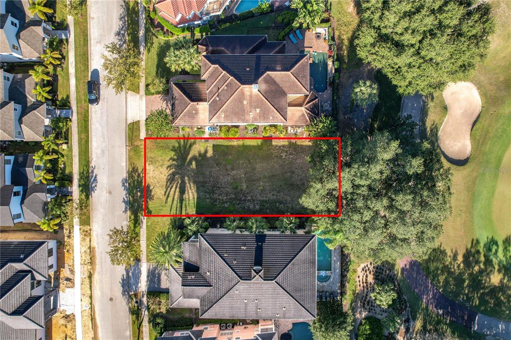 An aerial view shows a vacant rectangular lot situated between two large residential homes — 7455 GATHERING DRIVE, KISSIMMEE, FL