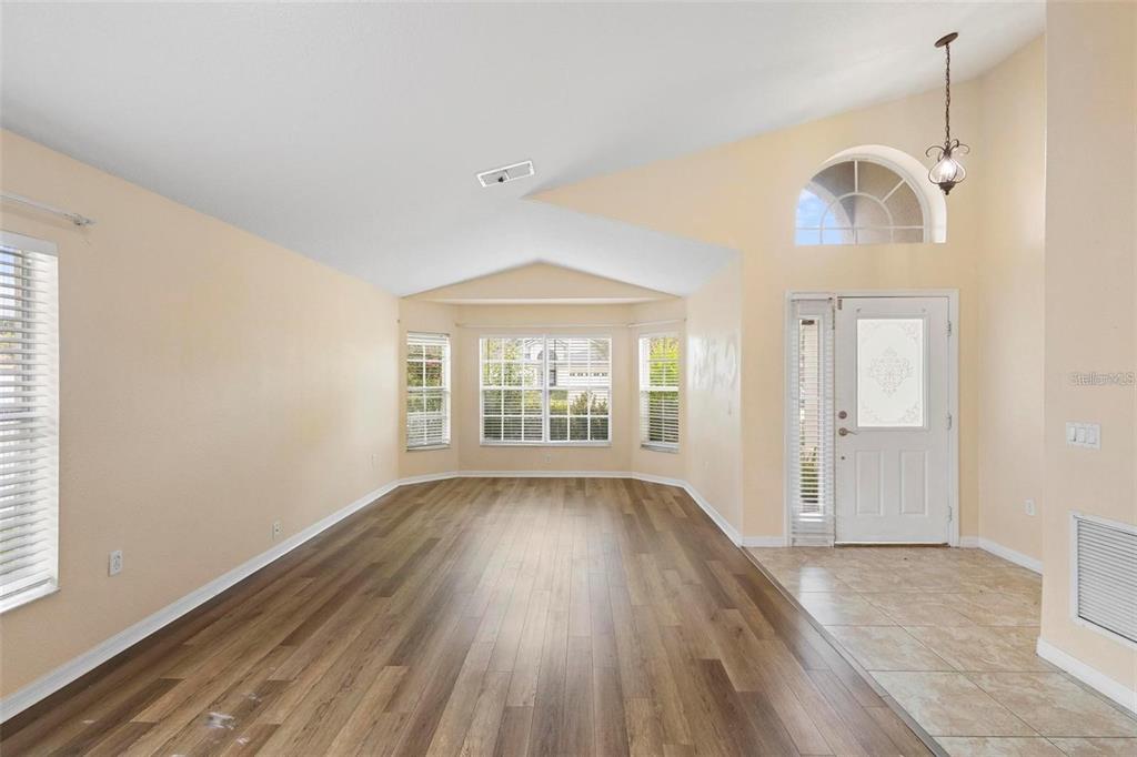 An empty living room features vaulted ceilings, wood-look flooring, and a front entryway with tile — 3152 WOOD ROSE WAY, DELTONA, FL