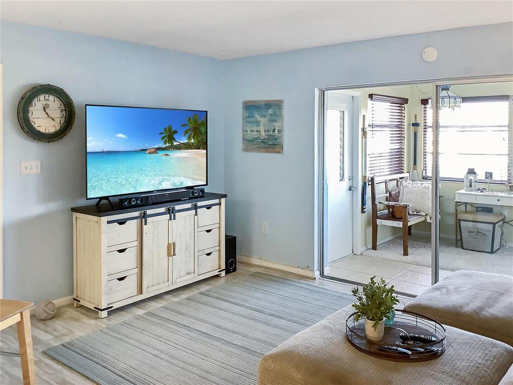 A living room features light blue walls, a television on a rustic console, and a sunroom — 4736 JASPER DRIVE UNIT 207, NEW PORT RICHEY, FL