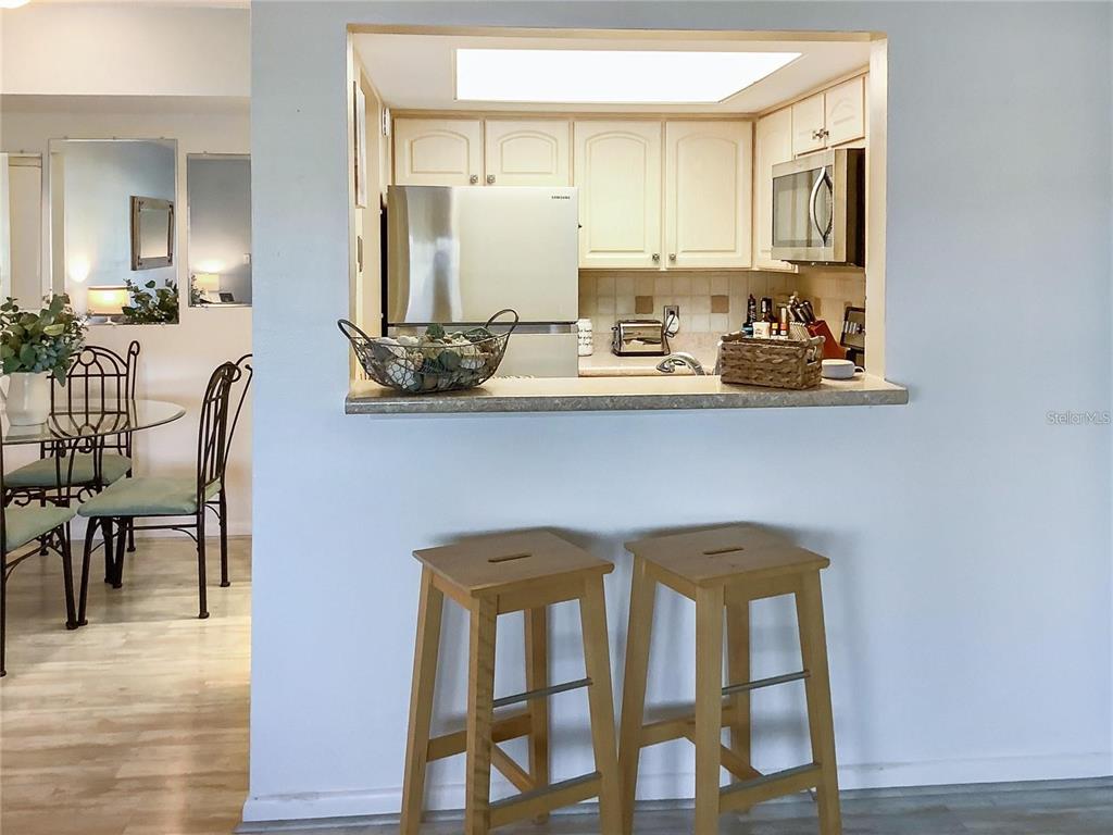 A kitchen with white cabinets and stainless steel appliances overlooks a dining area with stools — 4736 JASPER DRIVE UNIT 207, NEW PORT RICHEY, FL