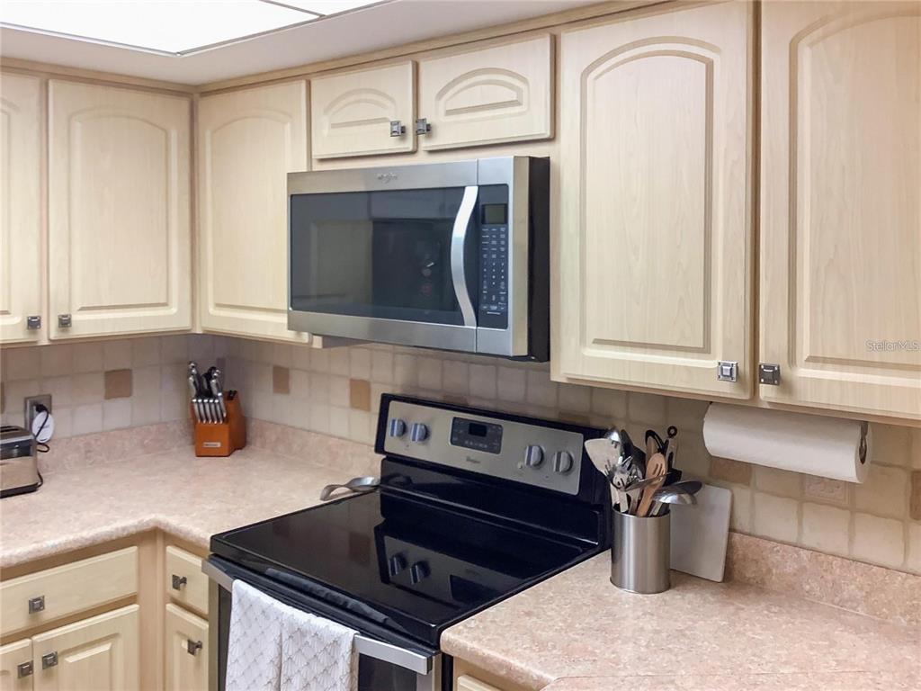 A kitchen features light wood cabinets, a stainless steel microwave, and a black electric stove — 4736 JASPER DRIVE UNIT 207, NEW PORT RICHEY, FL