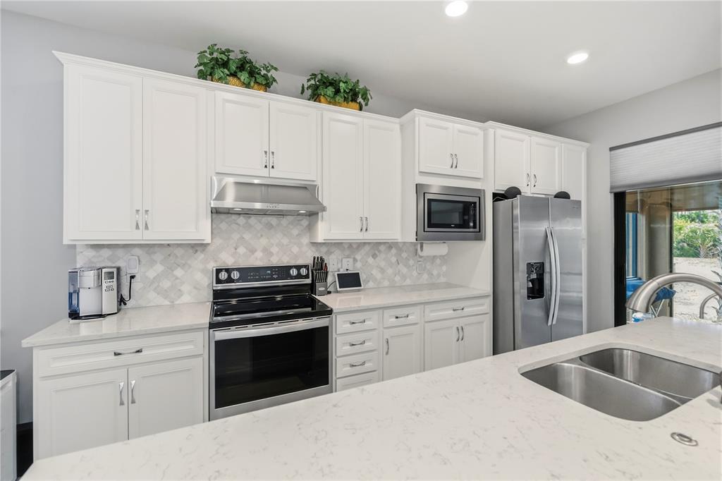 A modern kitchen features white cabinets, stainless steel appliances, and light-colored quartz countertops — 2475 BRASSICA DRIVE, NORTH PORT, FL