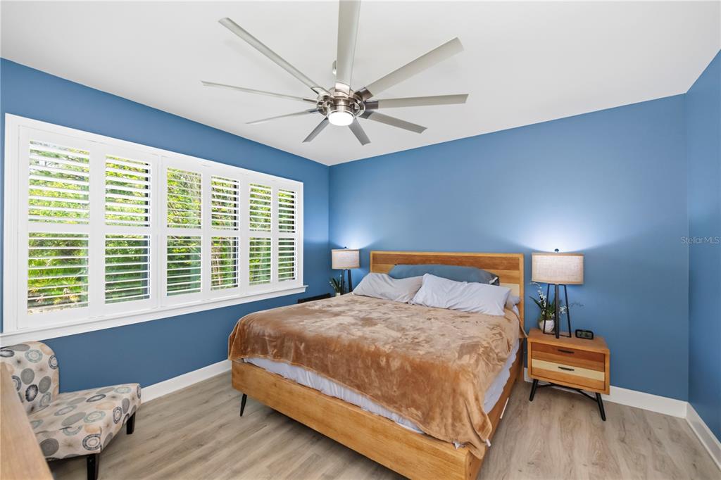 A bedroom features blue walls, a wooden bed frame, a ceiling fan, and white shutters — 2475 BRASSICA DRIVE, NORTH PORT, FL