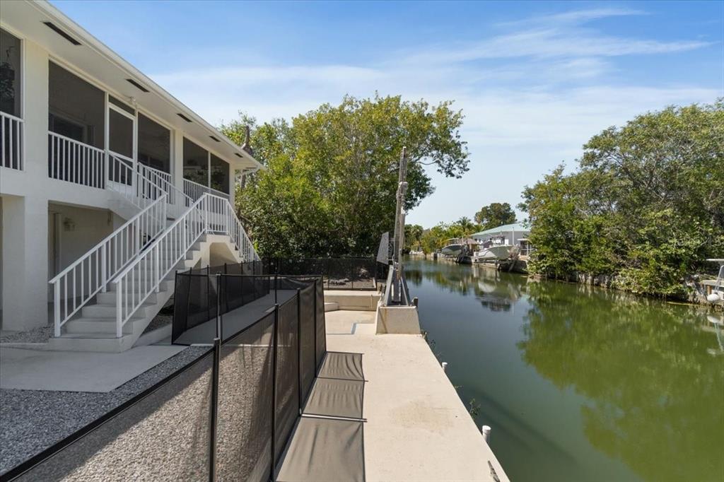 A white two-story house with a staircase overlooks a canal with a concrete dock — 29051 MAGNOLIA LANE, BIG PINE KEY, FL