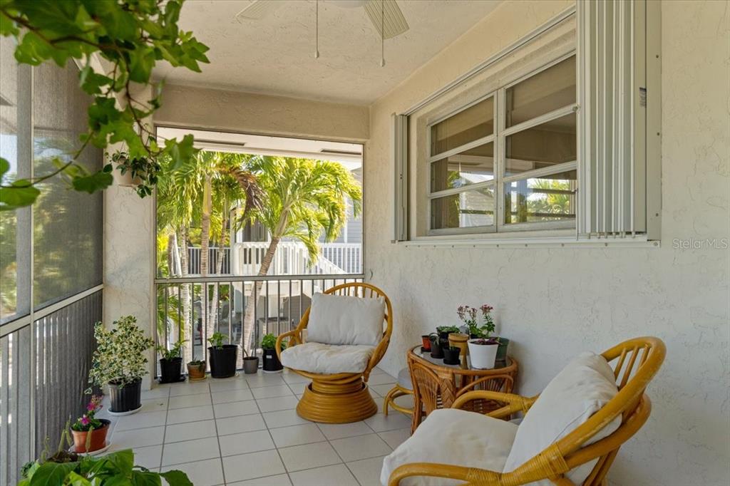A screened-in porch features tiled flooring, two wicker chairs, a small table, and potted plants — 29051 MAGNOLIA LANE, BIG PINE KEY, FL
