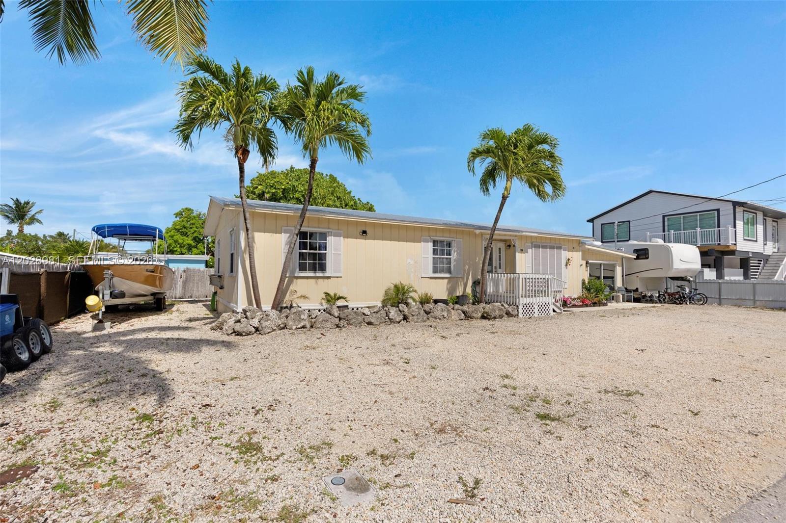 A single-story yellow house with palm trees and a gravel driveway sits under blue skies — 780 95th Street Ocean, Marathon FL 33050, MARATHON, FL